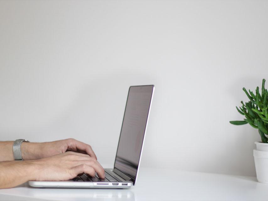 Hands working on a laptop at a bright, minimal desk